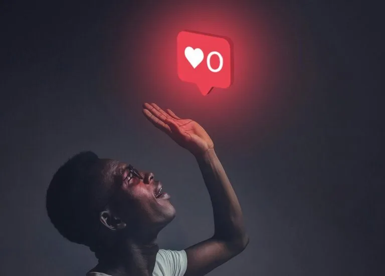 A man sits indoors reaching towards a glowing social media notification icon.